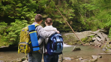 un par de turistas con mochilas admiran la hermosa cascada y la vista trasera del río de montaña