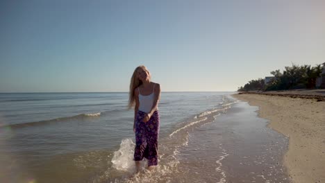 Wide-angle-slow-motion-of-joyous-mature-woman-backlit,-splashing-in-the-water-on-a-beach-at-sunrise-or-sunset