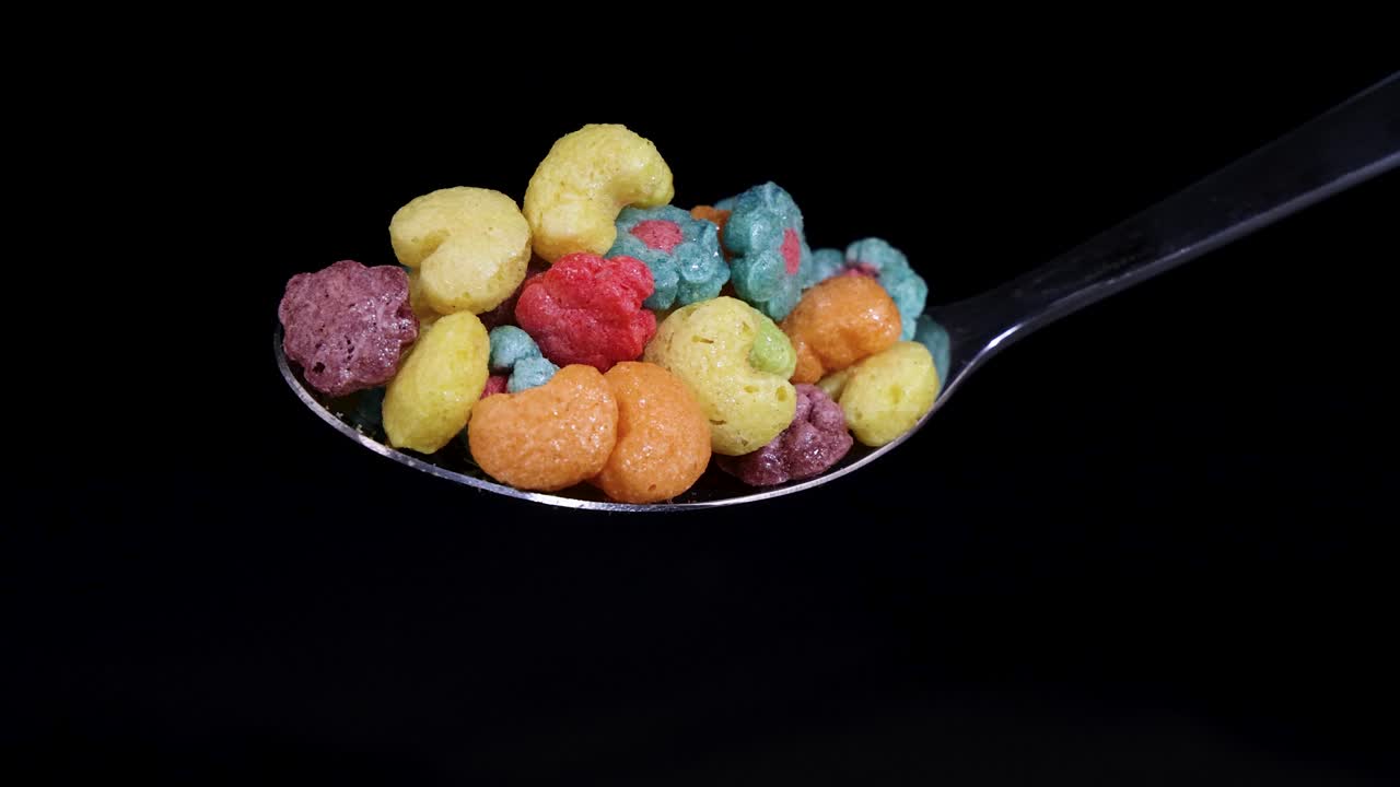 Vibrant cereal pieces drop from a spoon against a black background, captured in slow motion with dramatic lighting