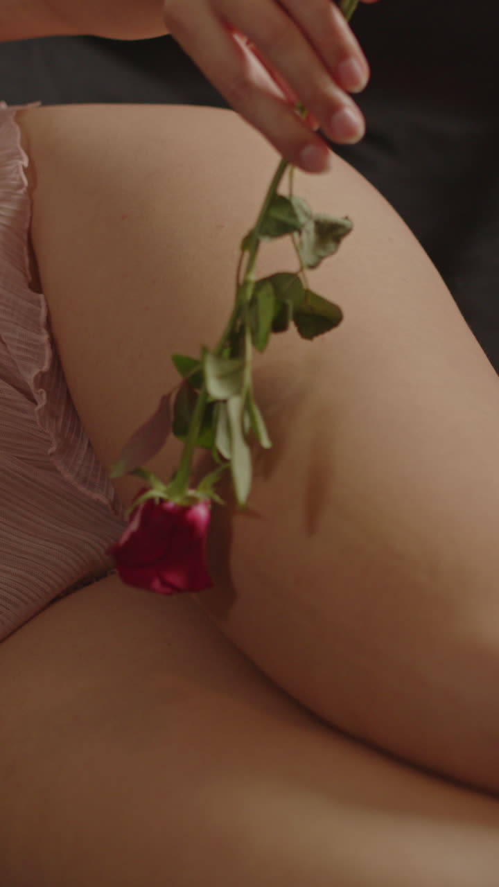 Bellissimo primo piano verticale di una rosa rossa che sfiora delicatamente la gamba di una bella donna in lingerie a letto