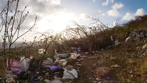 4k 60fps slow forwards fisheye dolly reveal of hilltop covered in plastic rubbish, trash and litter, ocean view of caribbean island