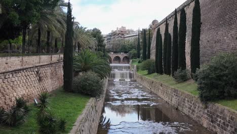 baluard de sant pere walls, riera river, bridge and cypress trees in palma de mallorca, spain next to the urban park