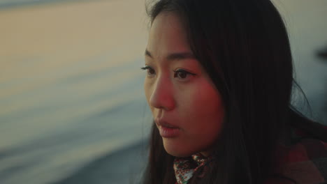 close-up of young pensive woman standing by lake in evening