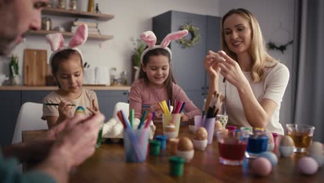 zoom in of caucasian family of four people chatting and decorating easter eggs in domestic kitchen.