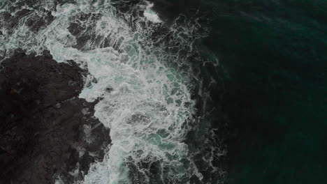 overhead view of deep aqua marine waves crashing over dark rocks on the west coast of scotland