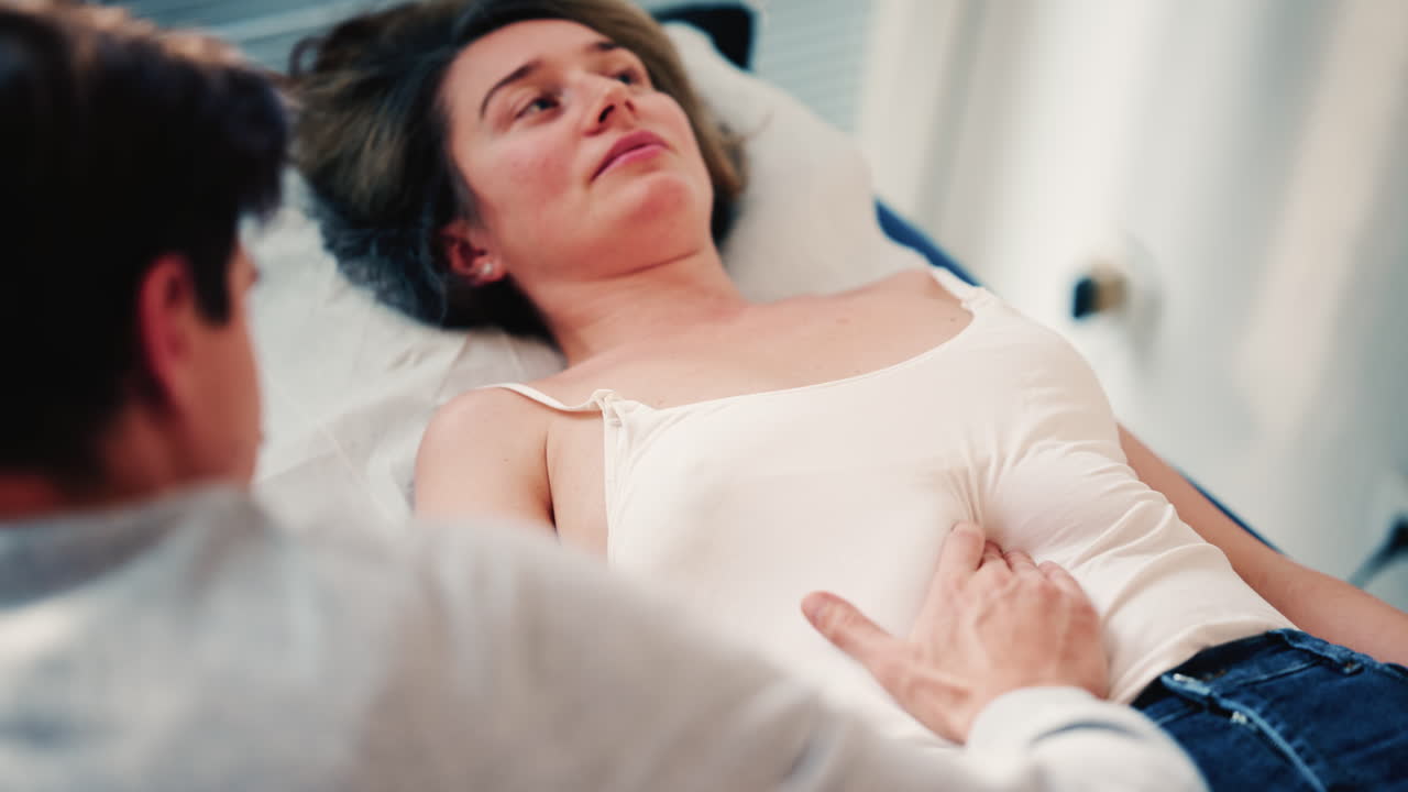 Terapeuta examinando a una mujer recostada en una cama médica, colocando las manos sobre el abdomen como parte de una evaluación o tratamiento