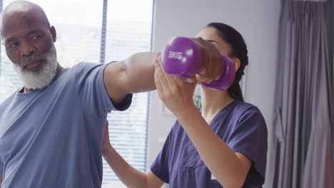 fisioterapeuta femenina diversa y paciente masculino de alto nivel sosteniendo una mancuerna en una sesión de fisioterapia