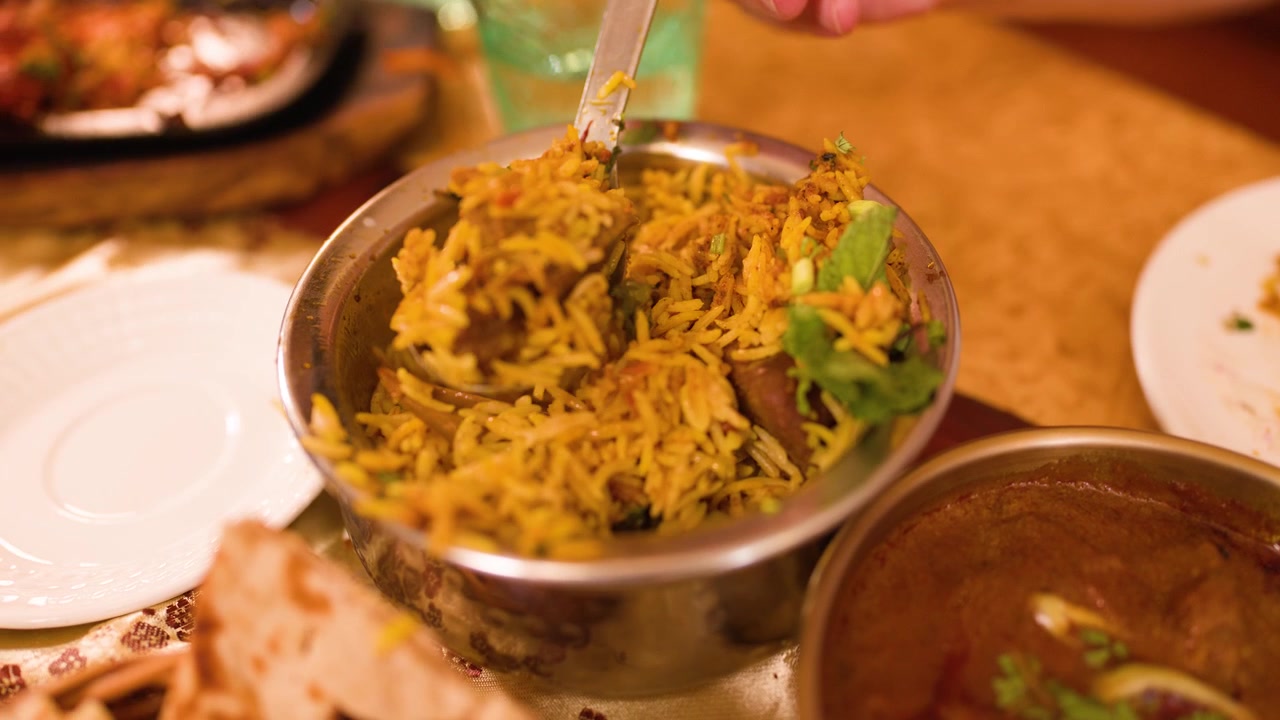 Primer plano de una cuchara sirviendo biryani de arroz basmati aromático de un cuenco metálico tradicional.