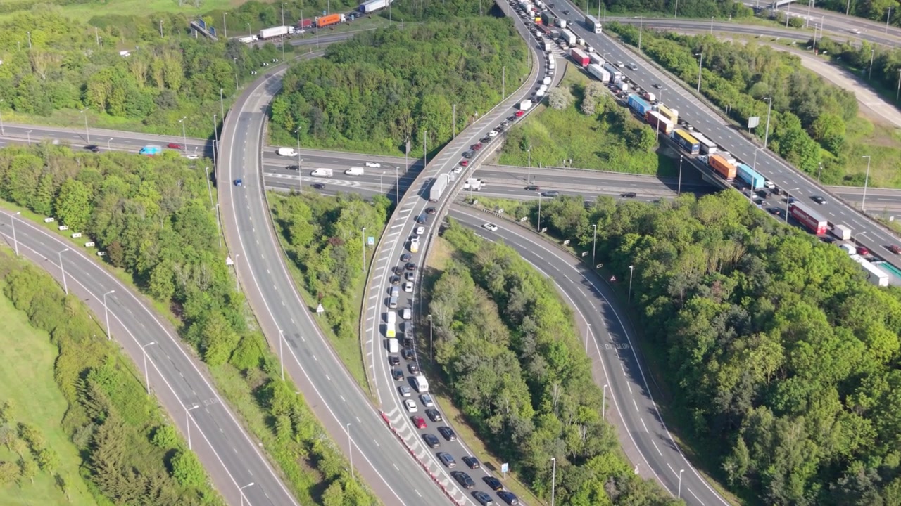 Çok şeritli bir otoyol kavşağının yoğun trafikle tıkandığı havadan görünüm. Parlak bir günde çok sayıda araba ve kamyon, birden fazla rampada ve yolda uzun kuyruklar oluşturuyor