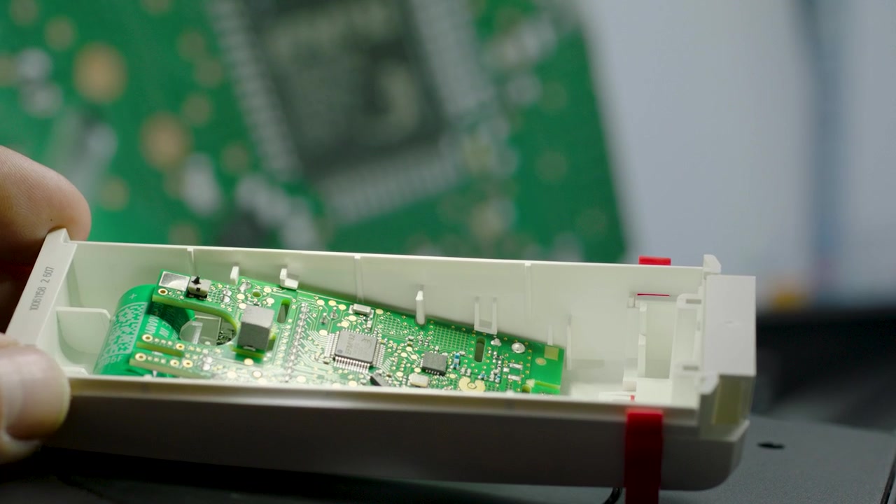 Mano che tiene un dispositivo elettronico aperto mostrando la scheda di circuito interna in primo piano