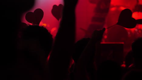 crowd of concertgoers holding heart-shaped signs in vibrant red lighting atmosphere