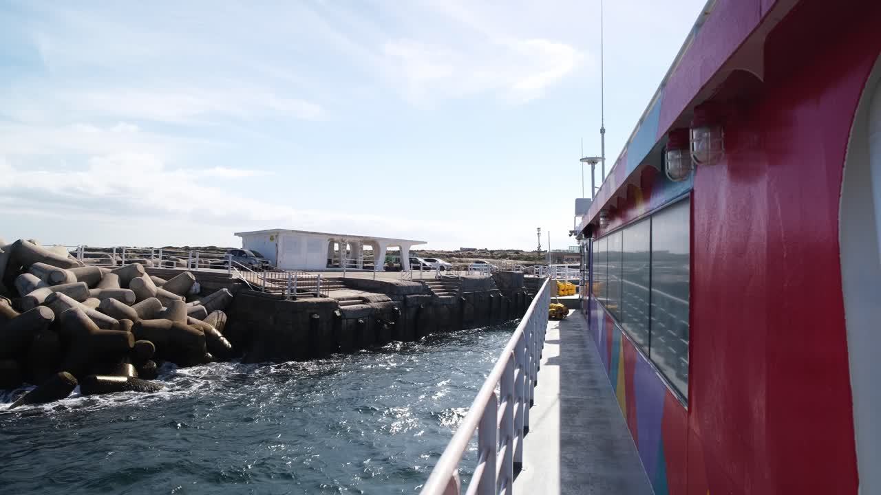 澄み渡る青空の下、波と岩場の港の景色を背景に加波島から出発するフェリーの風景。横長で撮影されたこのビデオは、韓国済州島の穏やかな交通手段を映し出しています。