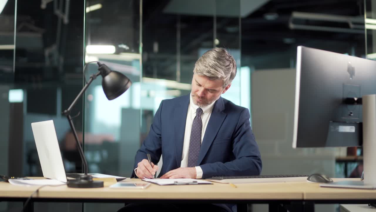 Senior business man signs a approval document in the office. Mature gray successful banker or lawyer businessman reading and signing business partnership contract