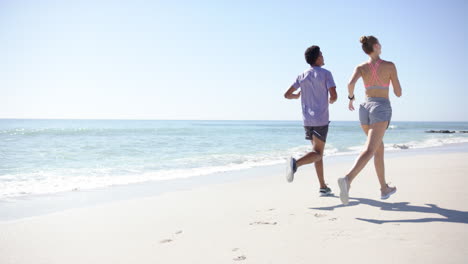 young biracial man and caucasian woman are jogging on a sunny beach with copy space