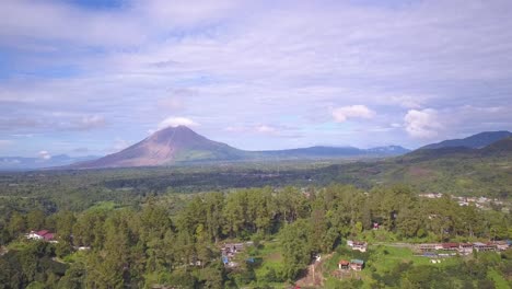 aerial footage flying over a beautiful green village towards mount sinabung volcano