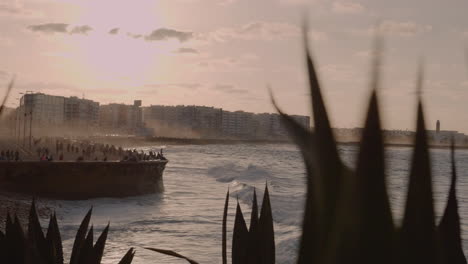 dynamic tight shot of casablanca morocco coast in the atlantic ocean, sunset over a partially cloudy sky, mist from the ocean, waves crashing, crowd watching, lots of people