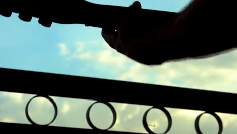 Silhouette-close-up-slo-mo-man-and-guitar-head-long-hair-waving-near-gate-with-blue-sky-and-cloud-background