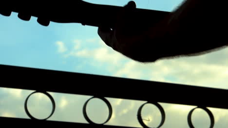 silhouette close up slo mo man and guitar head long hair waving near gate with blue sky and cloud background