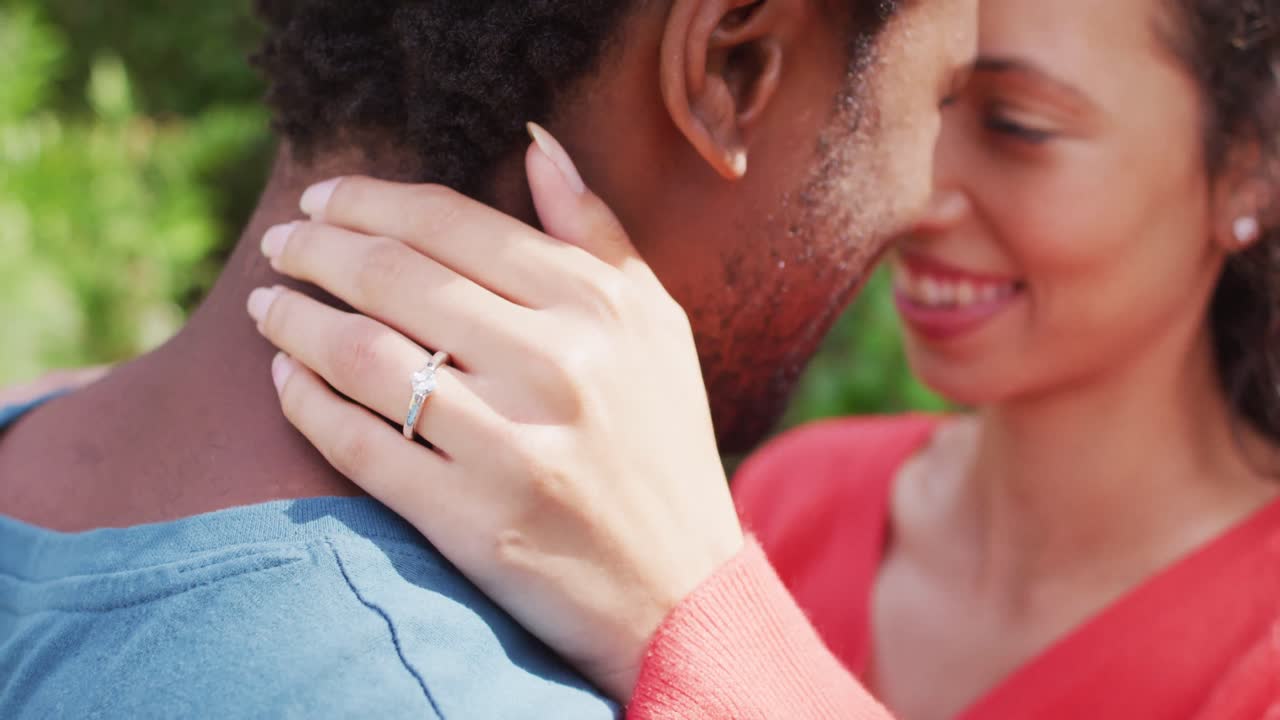 Close up of happy biracial woman with engagement ring on hand hugging to fiance