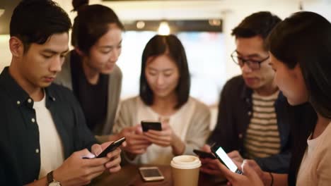 group of friends engaged in mobile technology interaction at a café, analyzing content on their smartphones in a social atmosphere