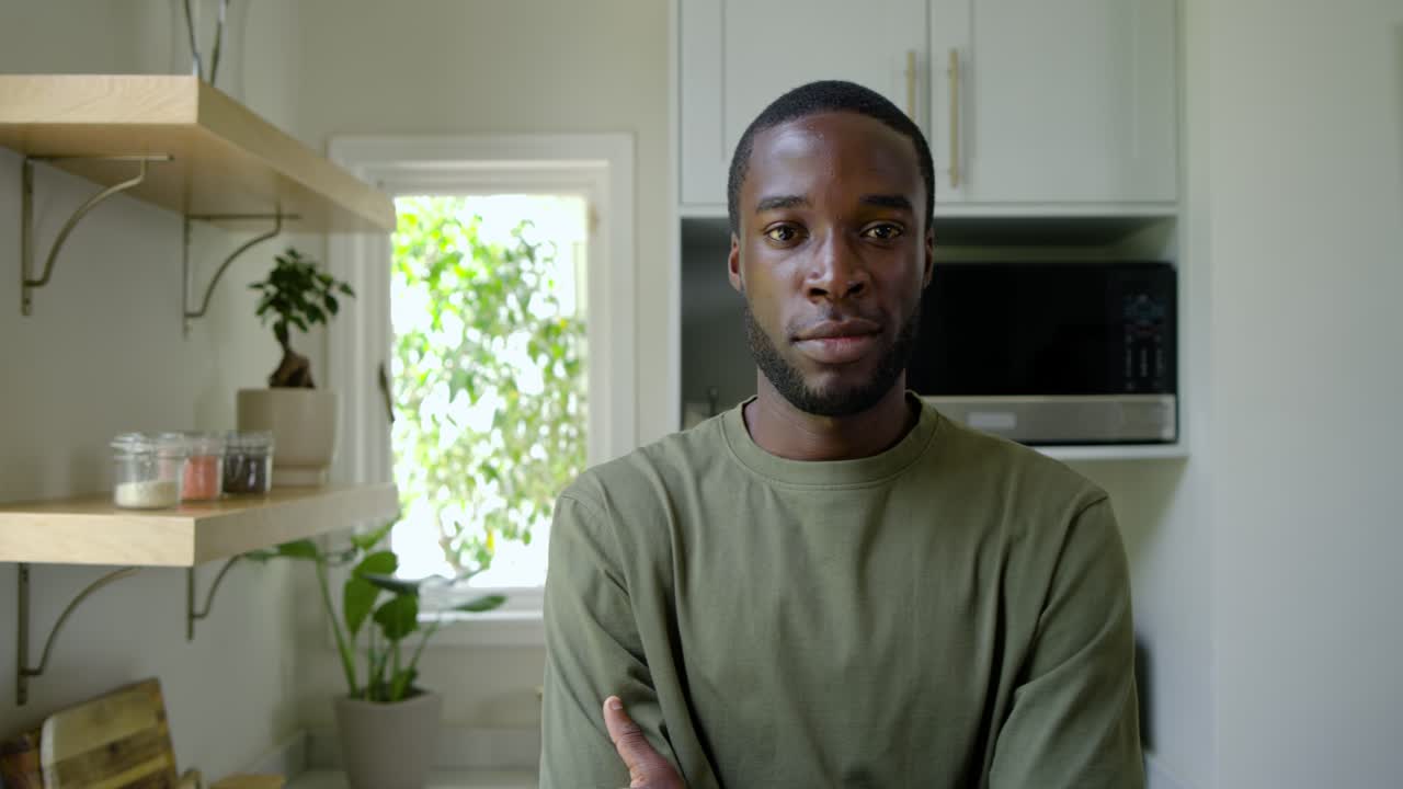 La telecamera inquadra un uomo afroamericano con una maglietta verde oliva che si gira sorridendo, mantenendo il contatto visivo con il microonde.