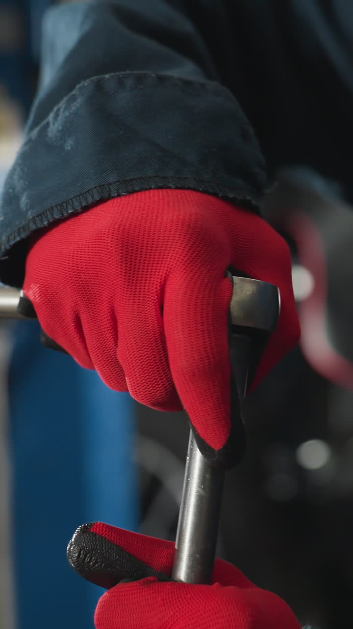 vista de cerca de la mano de la nuez mecánica de aflojamiento en el motor del automóvil con guantes rojos con fondo borroso del automóvil, herramientas mecánicas y entorno del taller