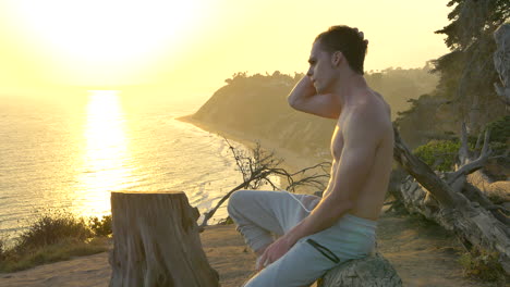 young attractive man resting after a cardio workout on the edge of a cliff above the pacific ocean during a golden sunset in santa barbara, california