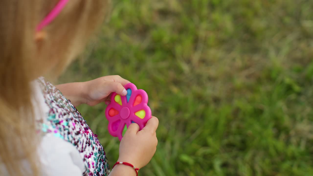 primer plano de una niña jugando a girar con pop it juguete sensorial contra el estrés en el parque, alivio de la ansiedad por estrés