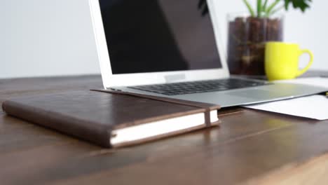 computadora portátil, cuaderno y taza de café dispuestos en una mesa de madera