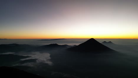 drone view in guatemala flying over a volcano crater volcano mountains in the horizon at sunrise covered by mist