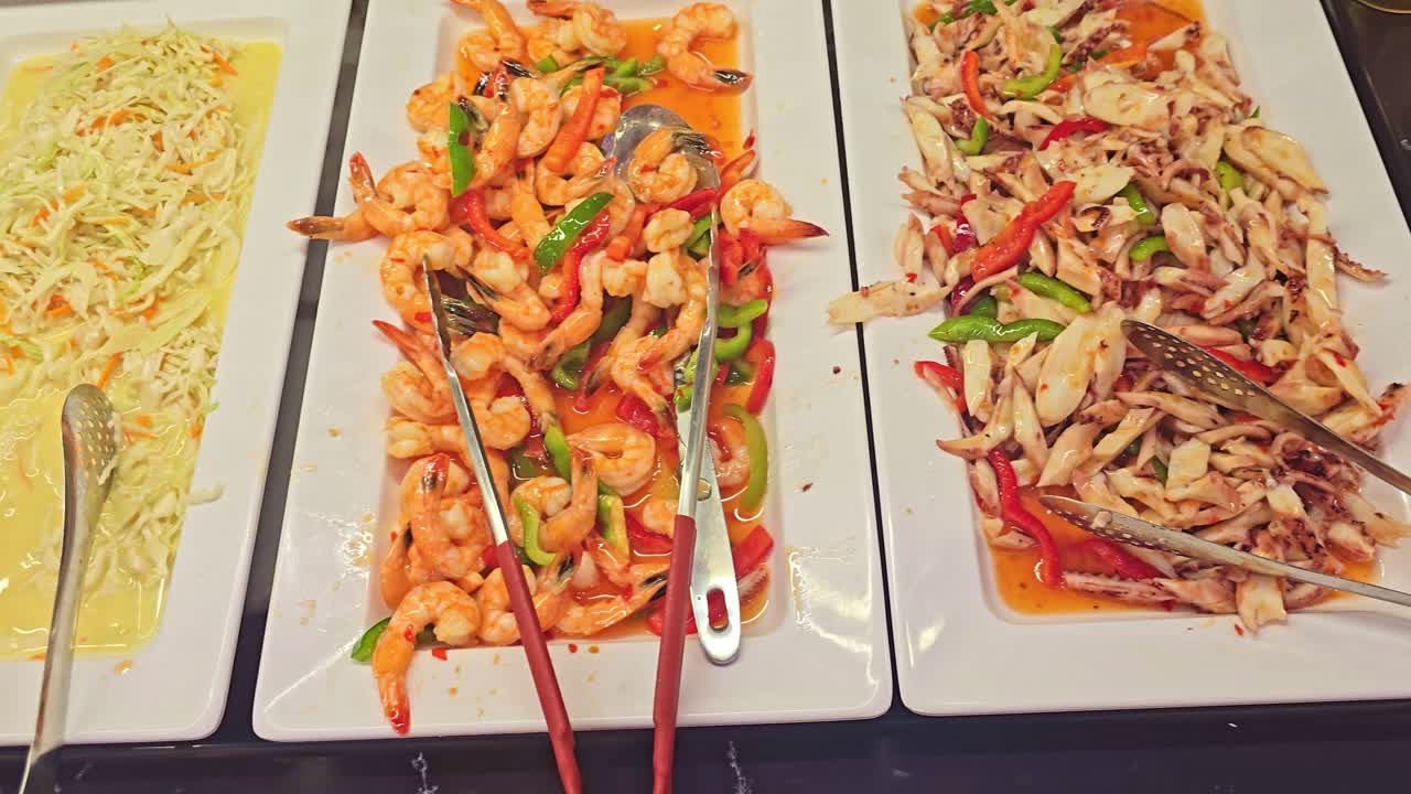 Panning close-up of a restaurant buffet showing shrimp, vegetable salad, and other dishes displayed on white trays