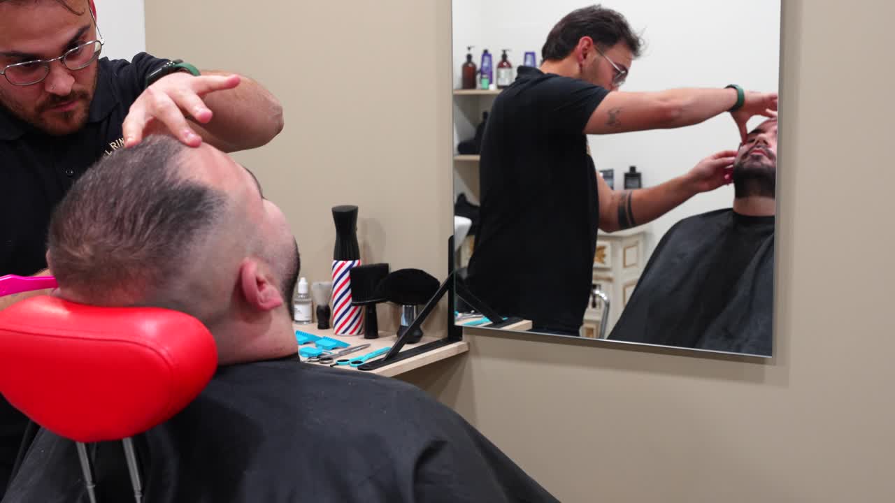 Barbiere bagna la lama del rasoio per ammorbidire la pelle e ridurre i tagli prima di radere il cliente nel negozio, preparazione lenta e accurata