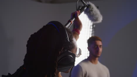 un equipo de filmación trabajando en un set, con un ingeniero de sonido sosteniendo una bomba de micrófono