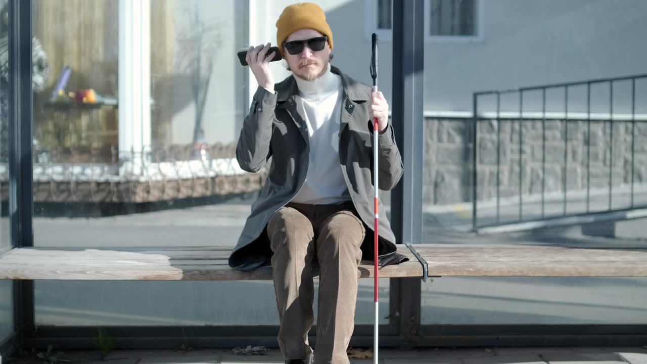 Visually impaired man talking on the phone, sitting on the bench in the city.