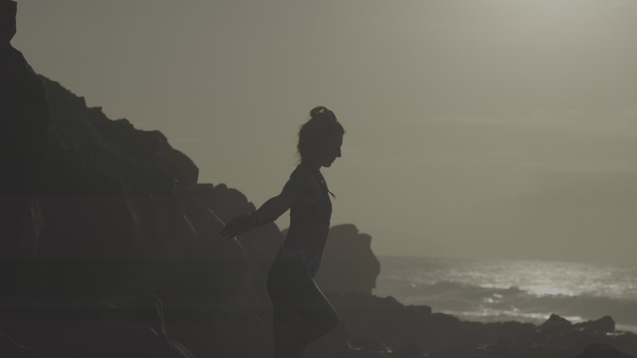 Woman practicing yoga on a rocky beach at sunset
