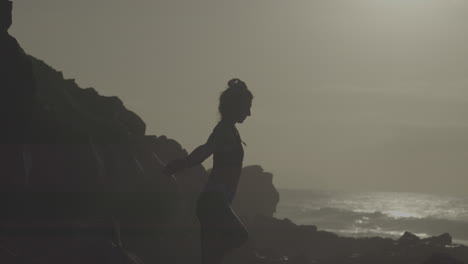 woman practicing yoga on a rocky beach at sunset