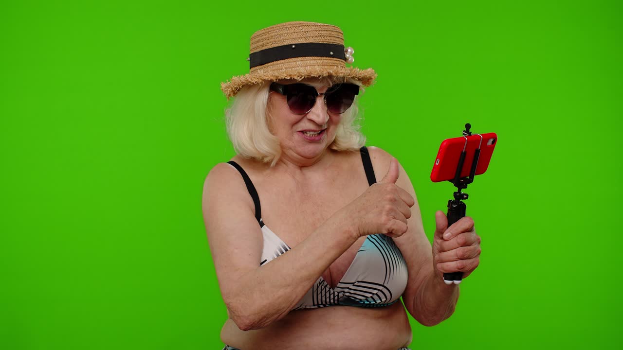 성숙한 여성 여행자 블로거가 휴대 전화로 셀피를 찍고 가족과 온라인 비디오 통화를 합니다.