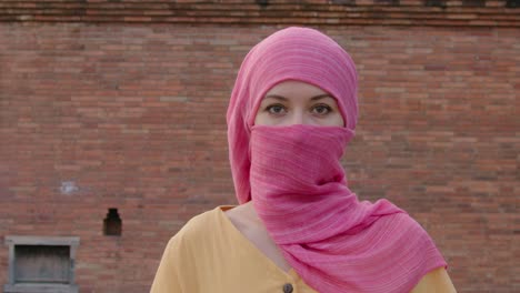 woman in pink hijab in front of brick wall