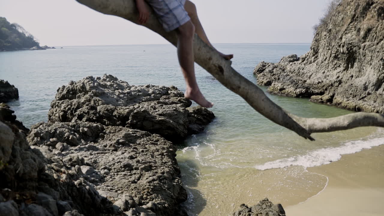 el hombre se relaja en el árbol en la rama con la playa del océano en el fondo, cámara lenta
