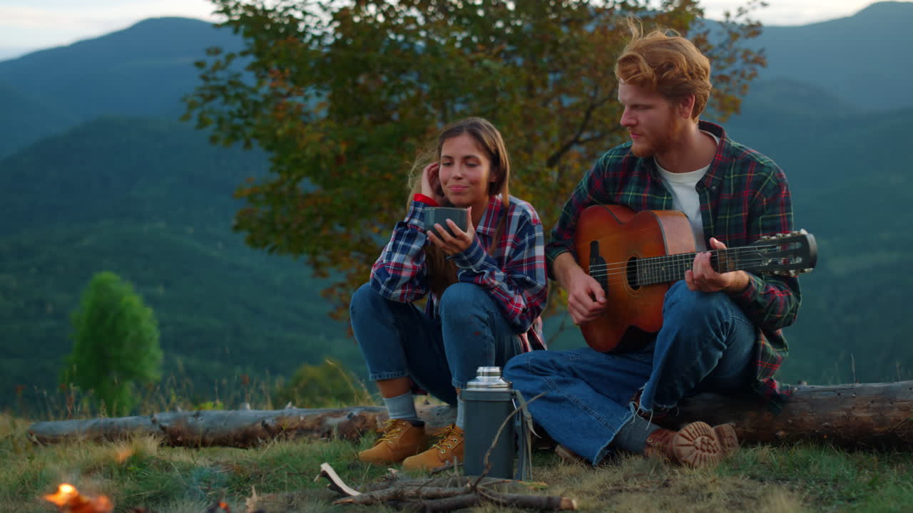 Afslappede kærester spiller guitar med udsigt til naturen. Et vandrepar holder ferie udendørs.
