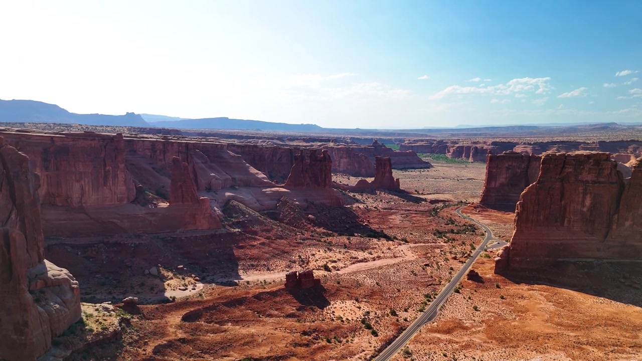 Splendido filmato stock del Parco Nazionale di Arches, USA, durante un pomeriggio luminoso. La luce solare brillante illumina le maestose strutture di arenaria rossa e il paesaggio desertico sotto un cielo azzurro limpido.