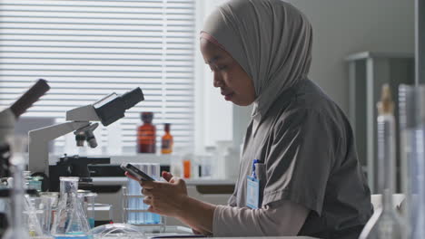 Female Researcher in Hijab Texting on Smartphone in Laboratory
