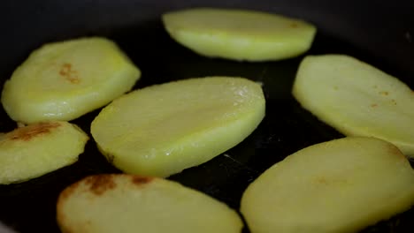 close up shot of thick potato slices being fried in a black pan