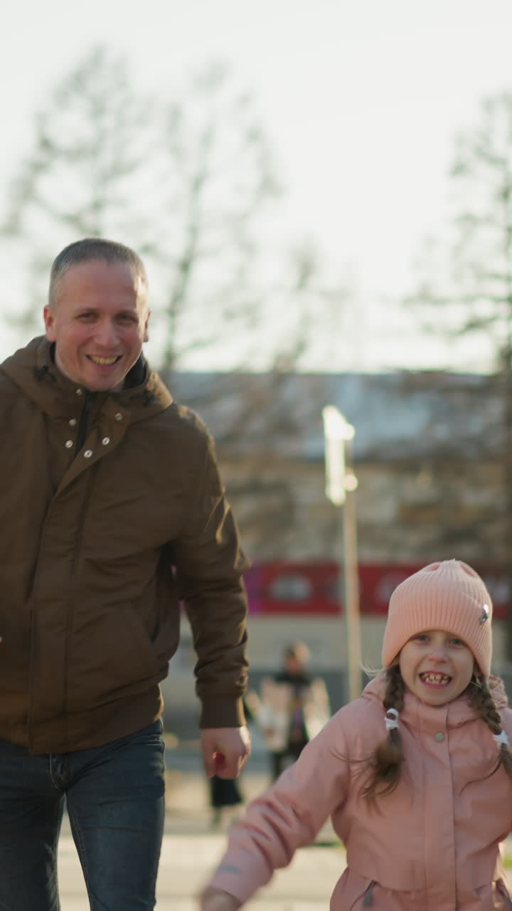 갈색 재과 파란 청바지를 입은 남자가 분홍색 모자와 재을 입은 웃는 어린 소녀와 함께 달리는 즐거운 장면