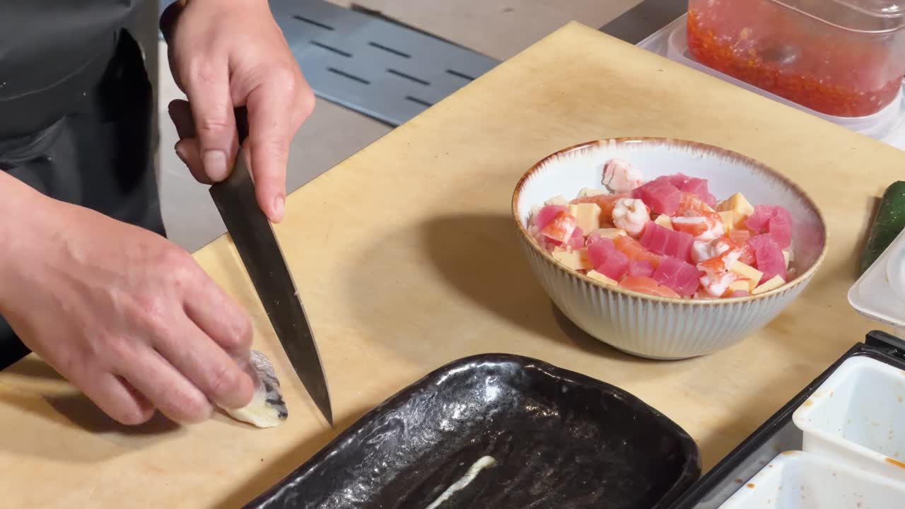 Close-up of chef slicing raw fish and assembling chirashi sushi bowl under bright lighting