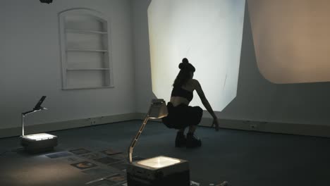 close view of woman in lotus position rises, moves towards the light, casting a shadow on the wall