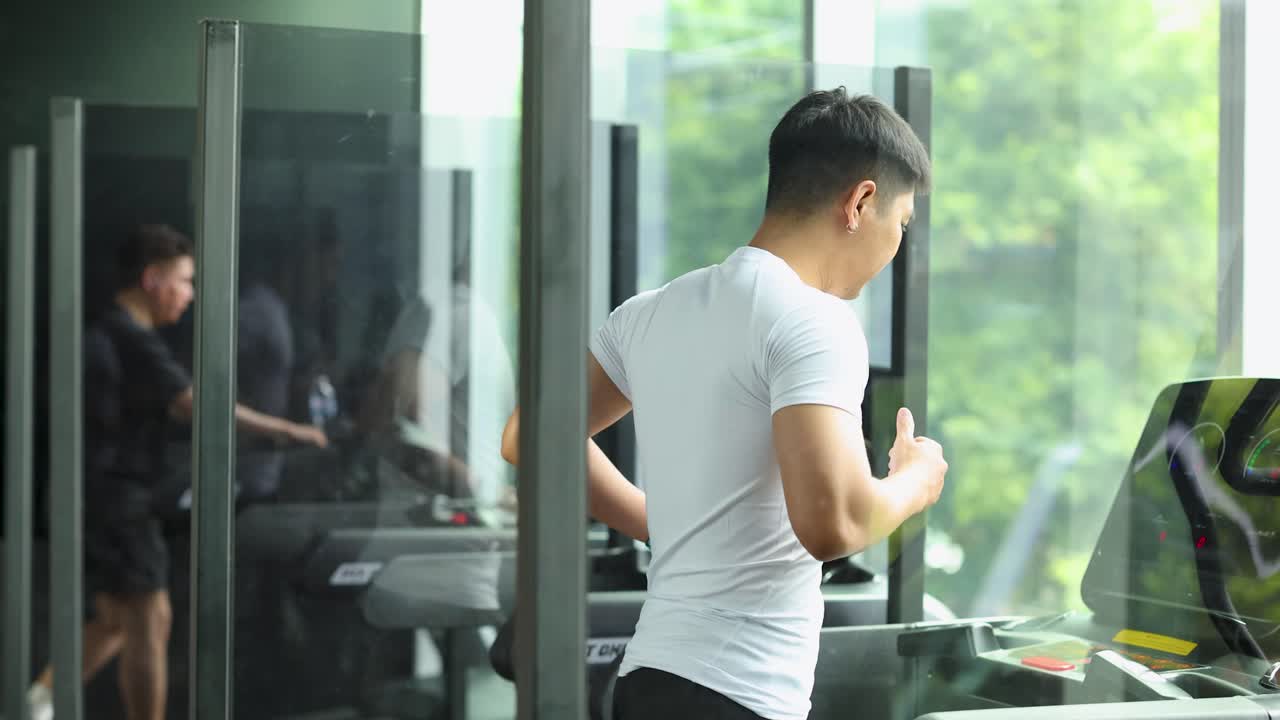 A man exercises on a treadmill in a bright, modern gym with large windows in Bangkok, Thailand