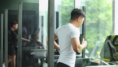 a man exercises on a treadmill in a bright, modern gym with large windows in bangkok, thailand