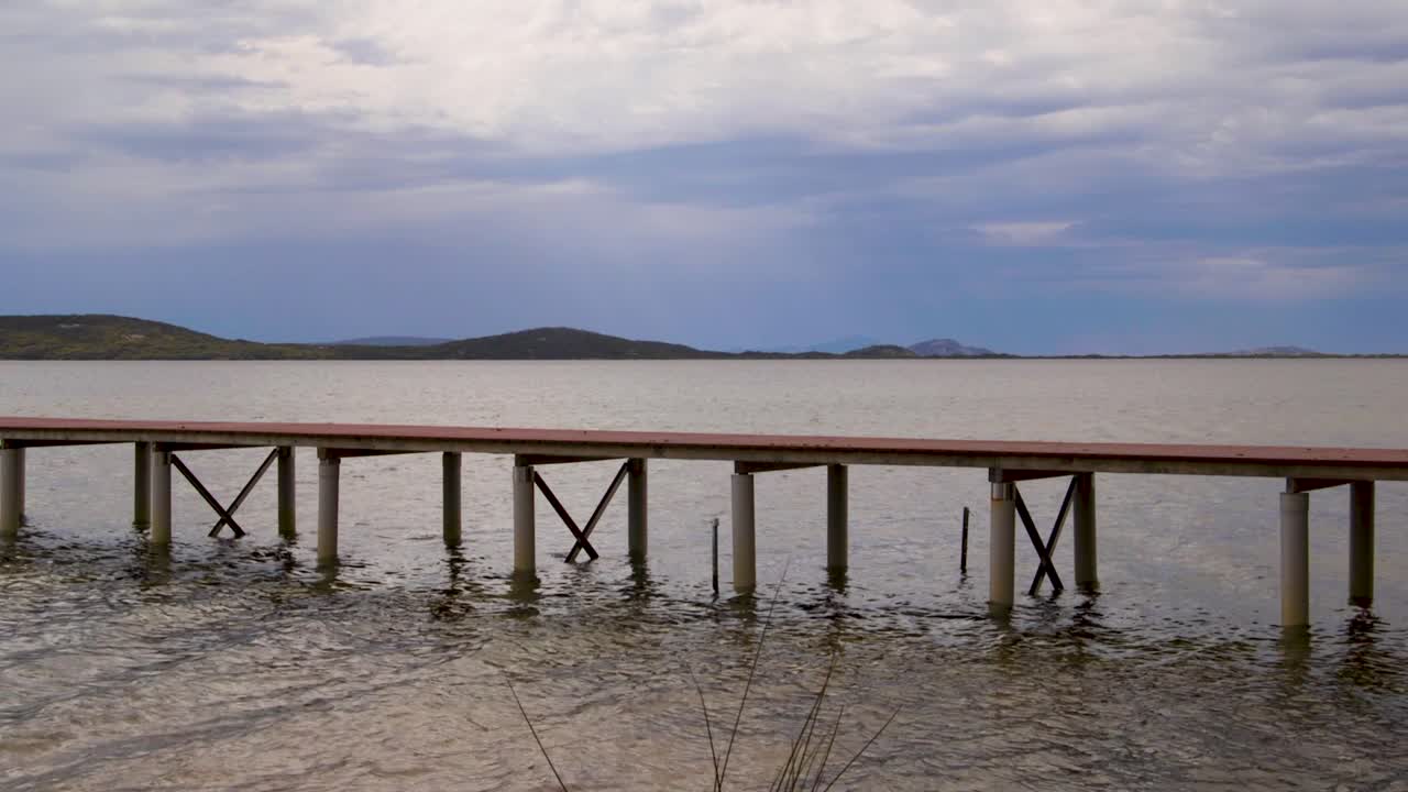 Un tranquillo pontile si estende su acque calme con uno sfondo di cielo nuvoloso, perfetto per annunci di viaggio o video di relax