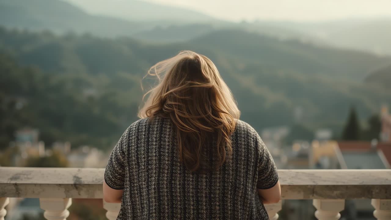 Leaning woman wearing patterned knit sweater on stone balcony, feeling breeze and taking in valley